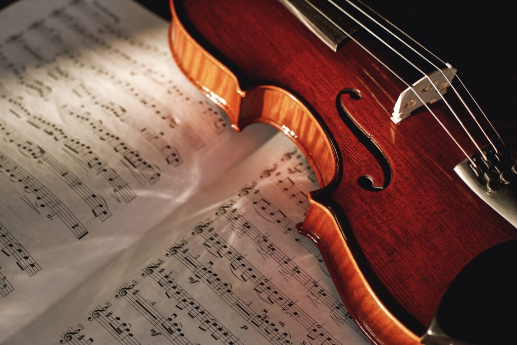 How to Read Violin Notes? Close up view of brown wood violin lying on the sheet with music notes.